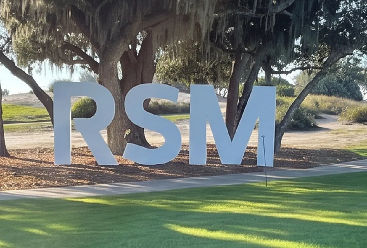 Very large free-standing three-dimensional letters set on a lawn beneath live oaks, forming a sponsor mark.