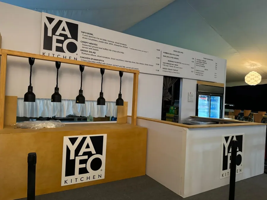 A timber service counter under pendant lights with a branded menu board above it and a printed sky-blue back wall.