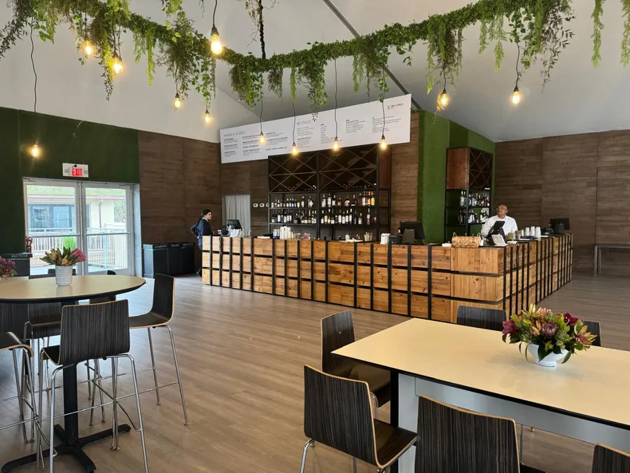 A long timber bar with a slatted screen behind it, trailing greenery and festoon lighting overhead, and tables set with flowers.