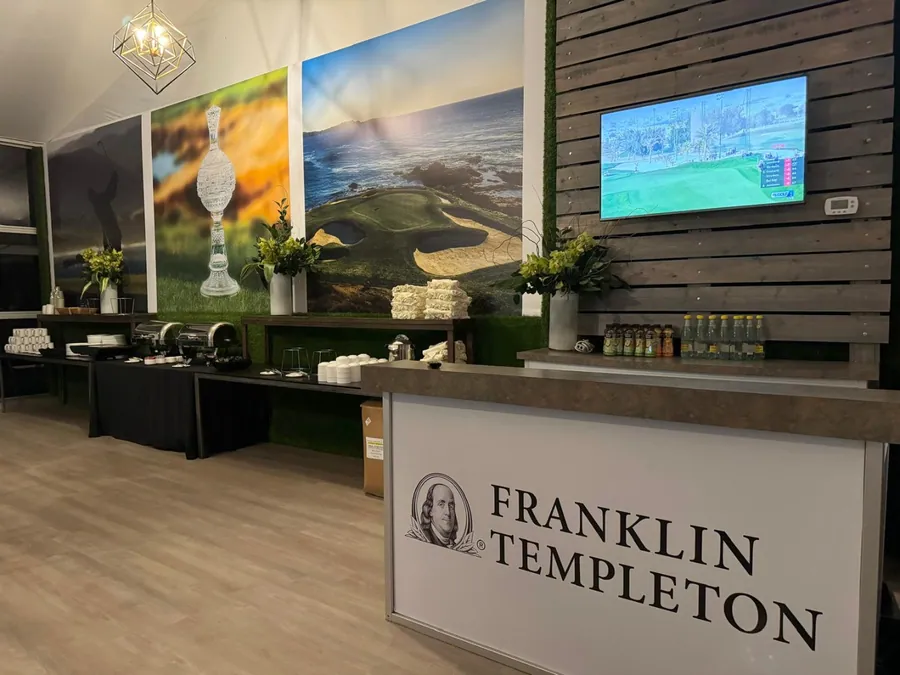 A dark timber bar with a preserved greenery panel above it, flanked by large framed golf prints and a wall-mounted screen.