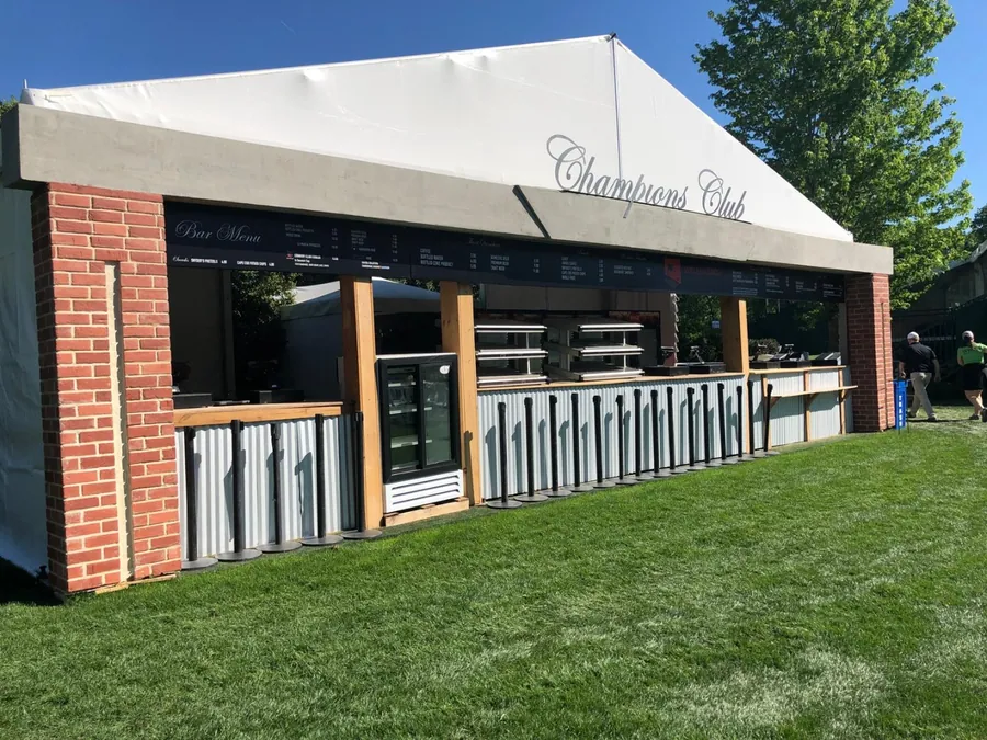 The exterior of a hospitality structure clad in brick and timber with a scripted roof sign, standing on a mown lawn.