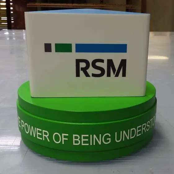 A branded tee marker block set on a green painted base on a tee box, printed with a sponsor mark and tagline.